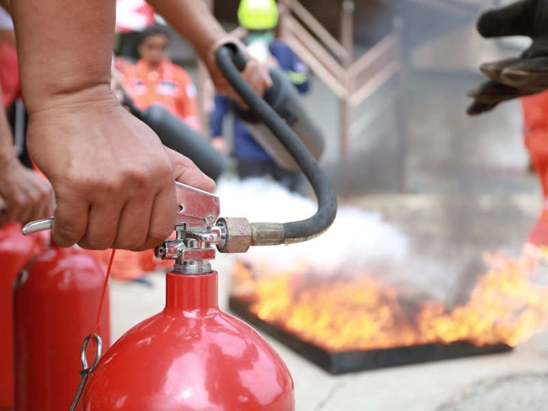 Hands using fire extinguisher on flames.