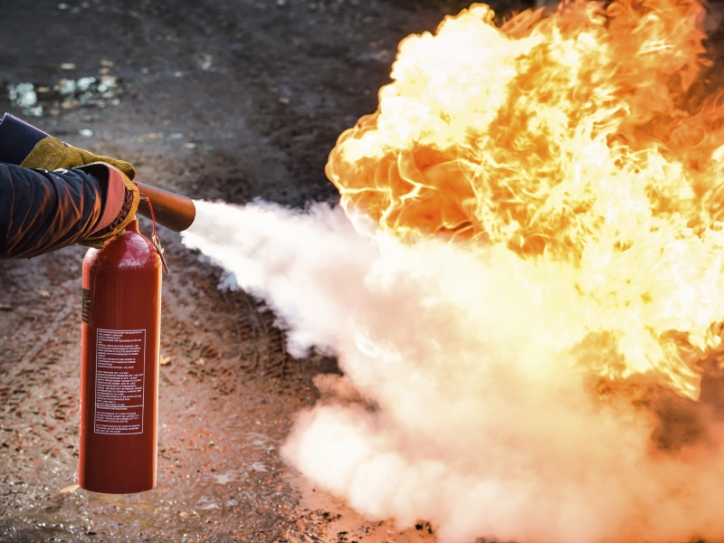 Here's an alt tag for the image: Person using fire extinguisher on blaze.